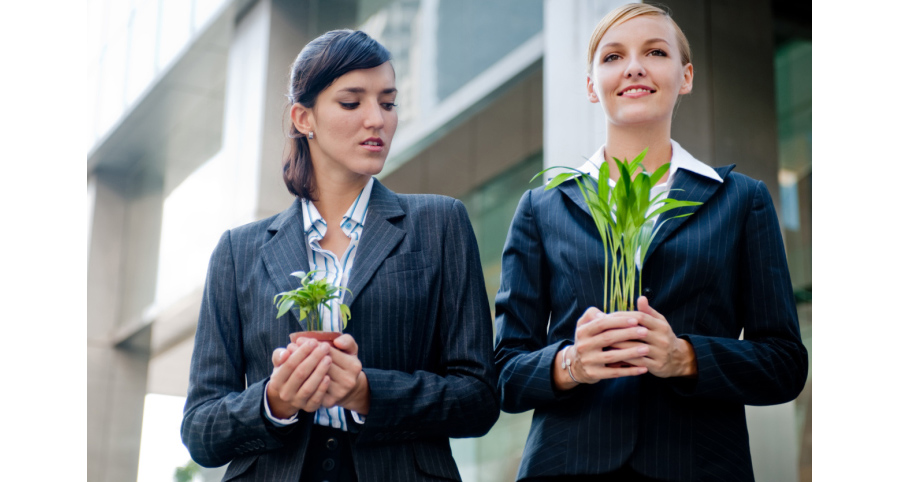 Two competitive businesswomen cupping their plants in their hands