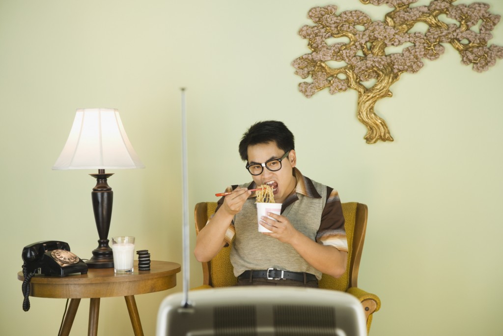 Nerdy Asian man eating in front of television